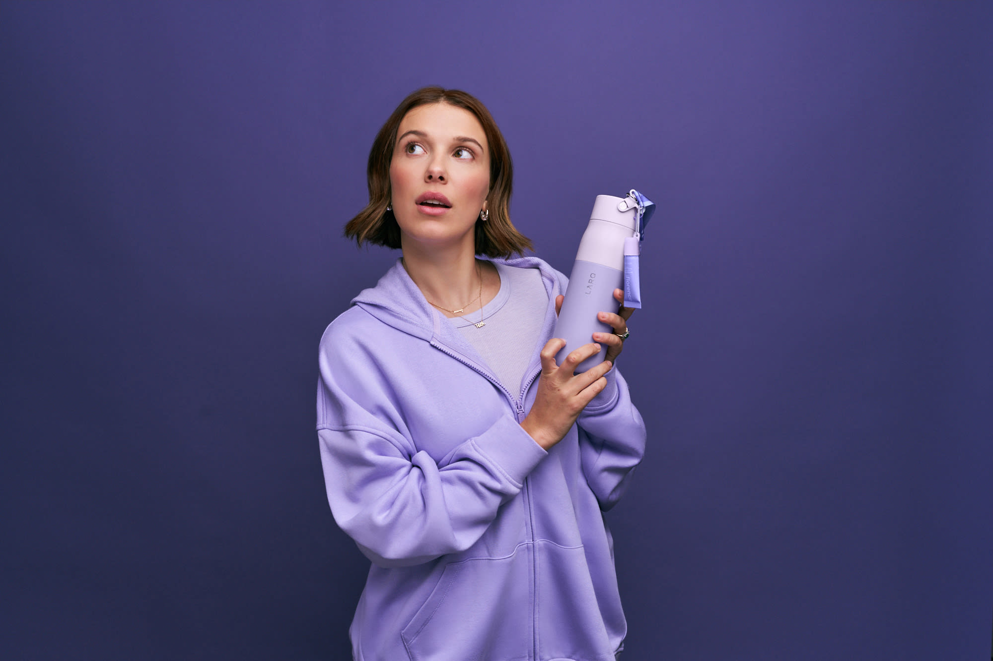 Millie Bobby Brown in a lavender hoodie holding the LARQ x florence by mills bottle